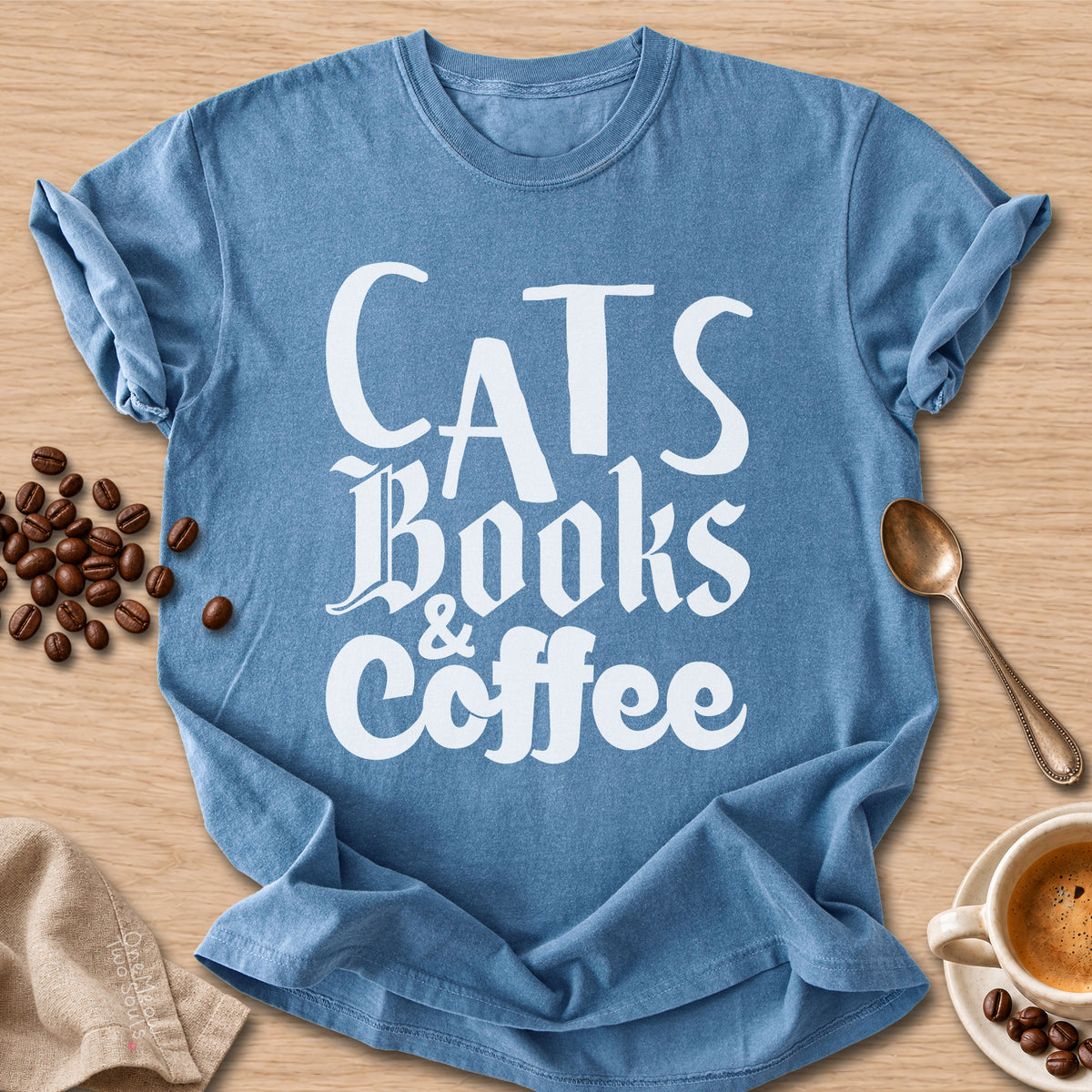 Blue Jean colored Comfort Colors 1717 cotton T-shirt, featuring a "Cats, Books & Coffee" funny cat design illustration. One Meow Two Souls brand.
