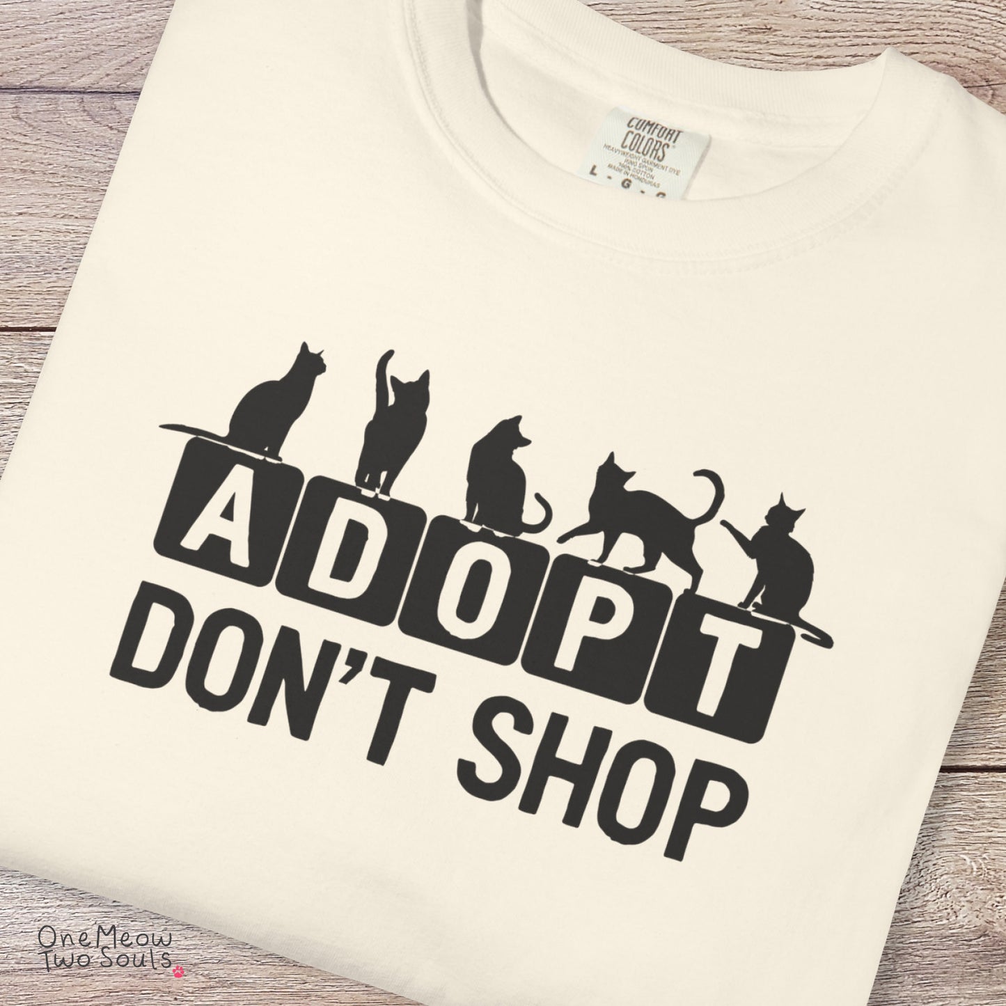 Ivory colored Comfort Colors 1717 cotton T-shirt, featuring a "Adopt Don't Shop" funny cat design illustration. One Meow Two Souls brand.
