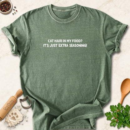 Moss colored Comfort Colors 1717 cotton T-shirt, featuring a "Cat hair in my food? It's just extra seasoning" funny cat design illustration. One Meow Two Souls brand.