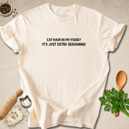 Ivory colored Comfort Colors 1717 cotton T-shirt, featuring a "Cat hair in my food? It's just extra seasoning" funny cat design illustration. One Meow Two Souls brand.