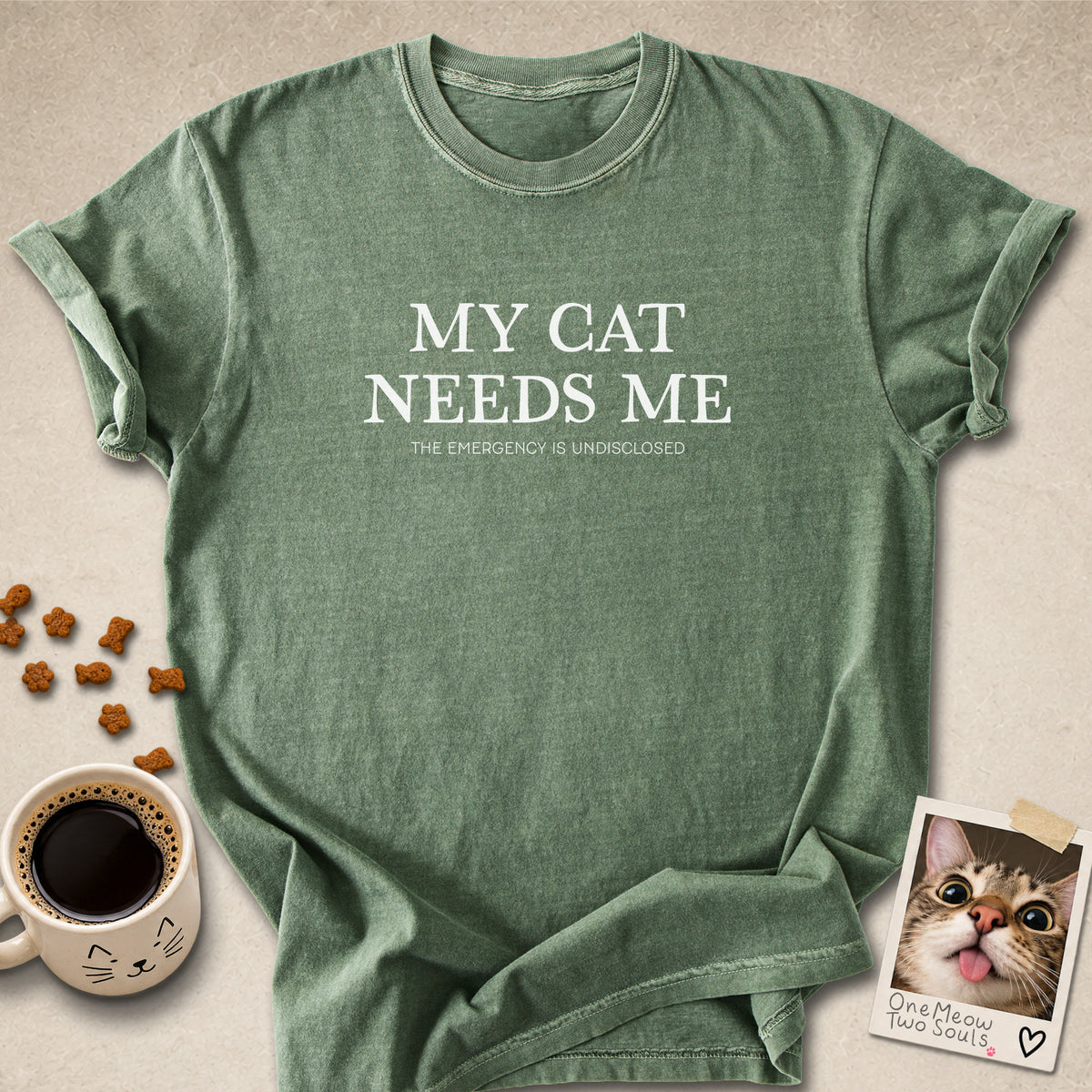 Moss colored Comfort Colors 1717 cotton T-shirt, featuring a "My Cat Needs Me. The Emergency is Undisclosed" funny cat design illustration. One Meow Two Souls brand.
