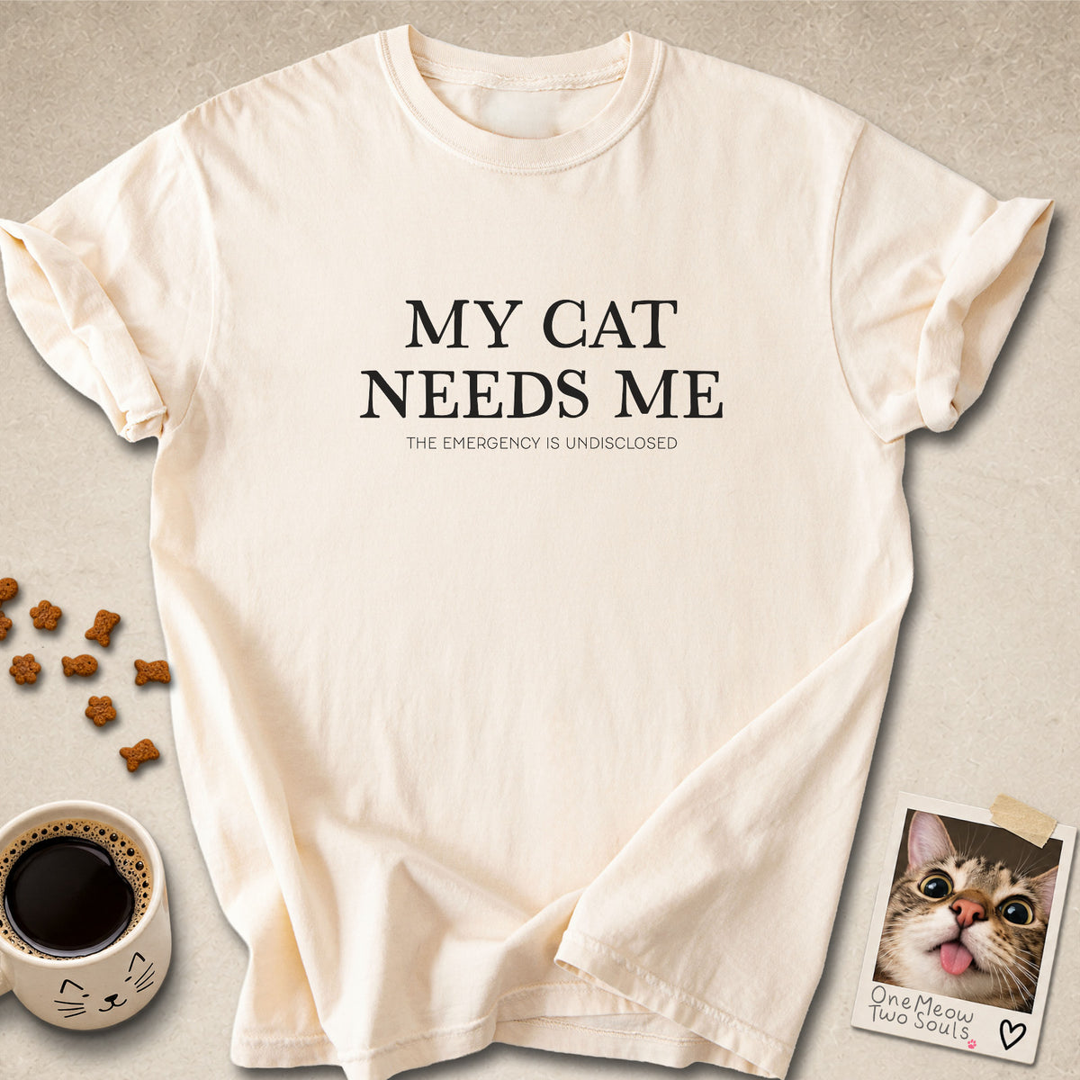 Ivory colored Comfort Colors 1717 cotton T-shirt, featuring a "My Cat Needs Me. The Emergency is Undisclosed" funny cat design illustration. One Meow Two Souls brand.