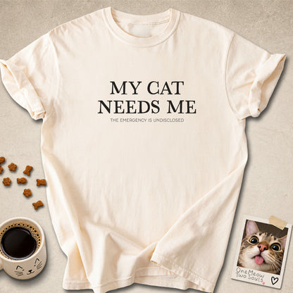 Ivory colored Comfort Colors 1717 cotton T-shirt, featuring a "My Cat Needs Me. The Emergency is Undisclosed" funny cat design illustration. One Meow Two Souls brand.