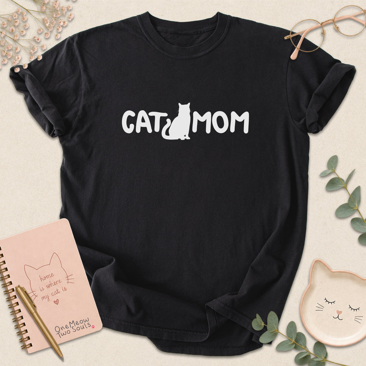 Black Comfort Colors 1717 t-shirt with a white graphic reading 'CAT MOM'. One Meow Two Souls brand.