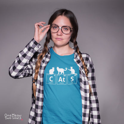 A young woman with braided hair and glasses wears a teal graphic t-shirt with a white cat-themed periodic table design, layered under a black and white plaid flannel shirt, against a solid gray studio background.
Sapphire colored Comfort Colors 1717 cotton T-shirt, presenting a "CatS" funny chemistry periodic table cat design. One Meow Two Souls brand.