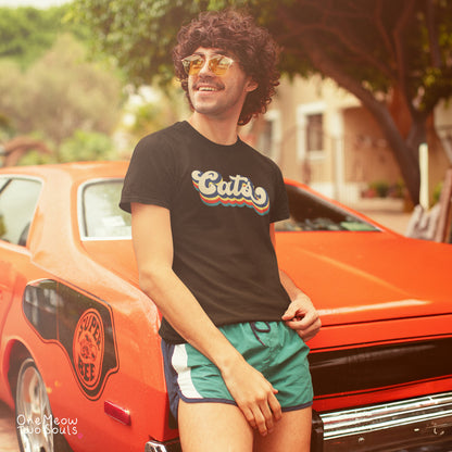 A man wearing a black graphic t-shirt with 'Cats' in retro white and orange lettering, teal shorts, and gold-tinted sunglasses, leaning against an orange classic car outdoors.
Black colored Comfort Colors 1717 t-shirt with a retro "Cats" typography design. Onw Meow Two Sould brand.