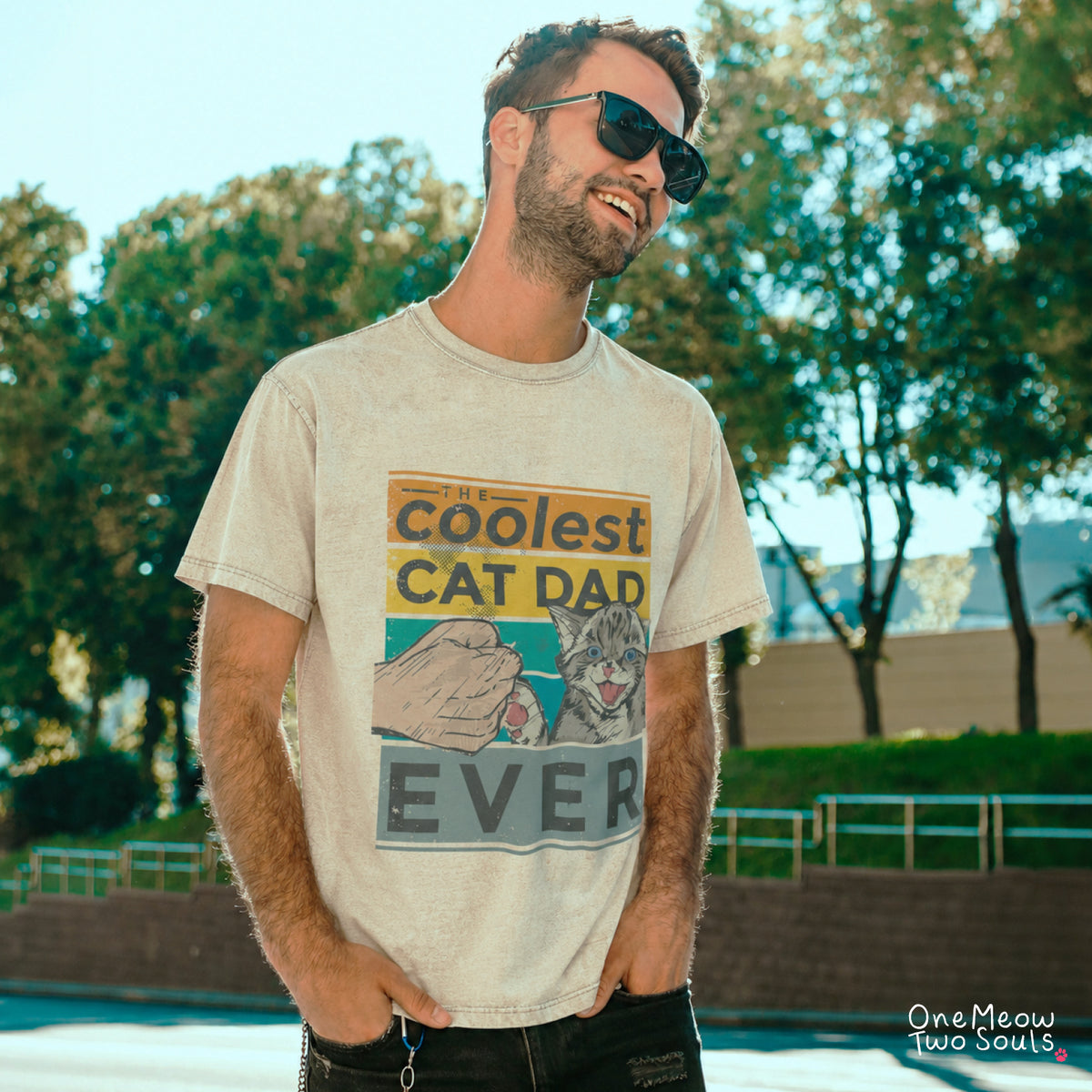 A man wearing a light beige graphic t-shirt that reads 'coolest CAT DAD EVER' with an illustration of a cat and a hand, standing outdoors in front of trees.
Ivory colored Comfort Colors 1717 T-shirt with a "The Coolest Cat Dad Ever" colorful retro design. One Meow Two Souls brand.