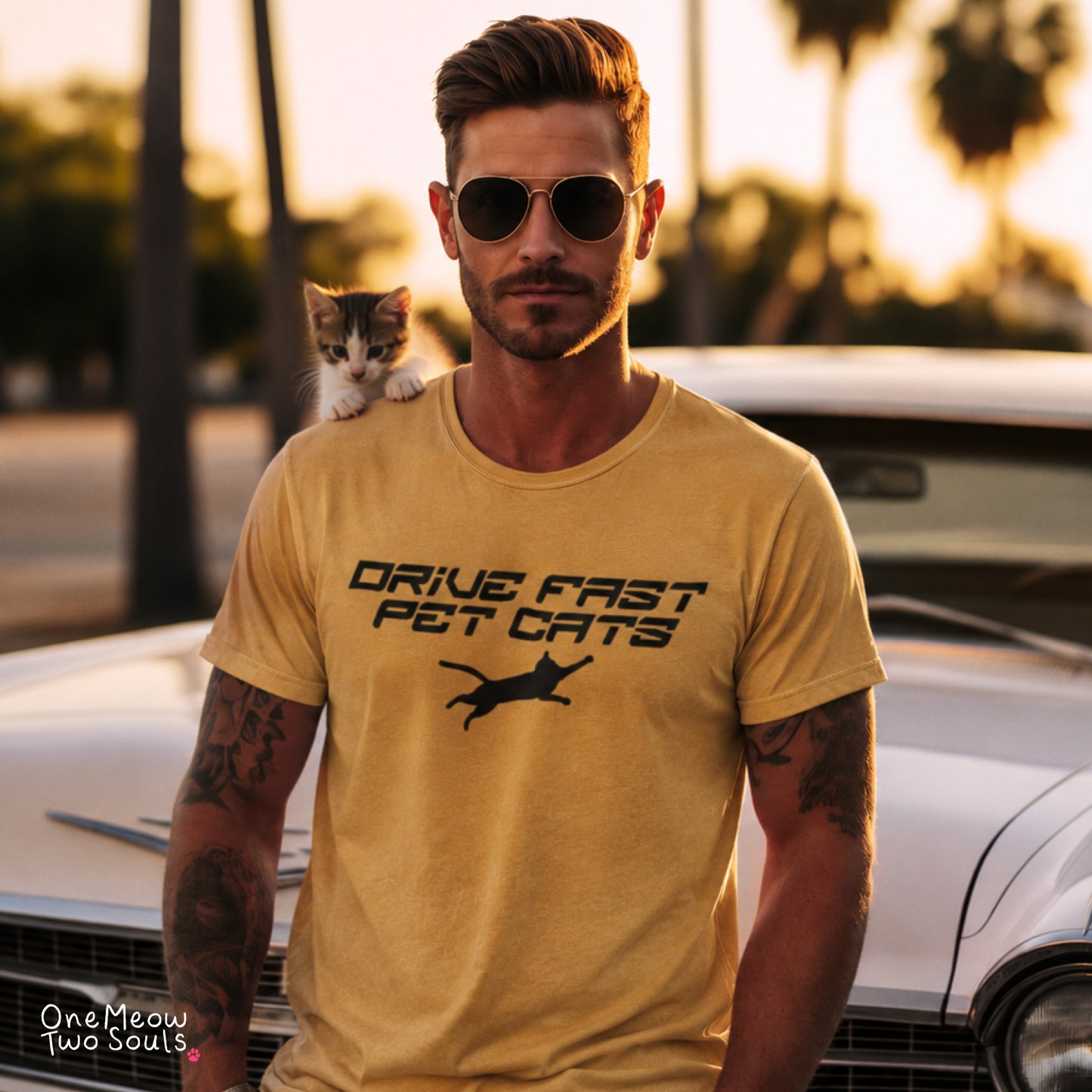A man wearing round sunglasses and a yellow graphic t-shirt with the text 'DRIVE FAST PET CATS' and a cat silhouette, standing in front of a white car with a small kitten on his shoulder. Mustard color Comfort Colors 1717 t-shirt with a "Drive Fast Pet Cats" design. Aimed for Cat dads and men who love cats. One Meow Two Souls brand.