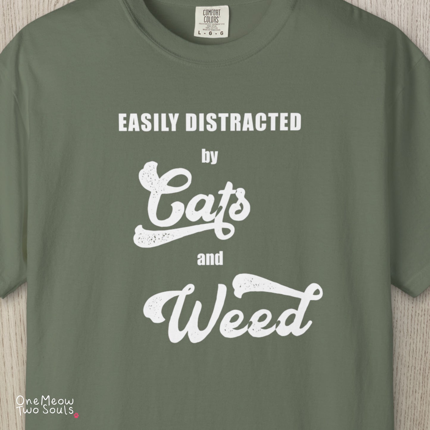 Moss colored Comfort Colors 1717 cotton T-shirt, featuring a "Easily Distracted by Cats and Weed" funny cat design illustration. One Meow Two Souls brand.