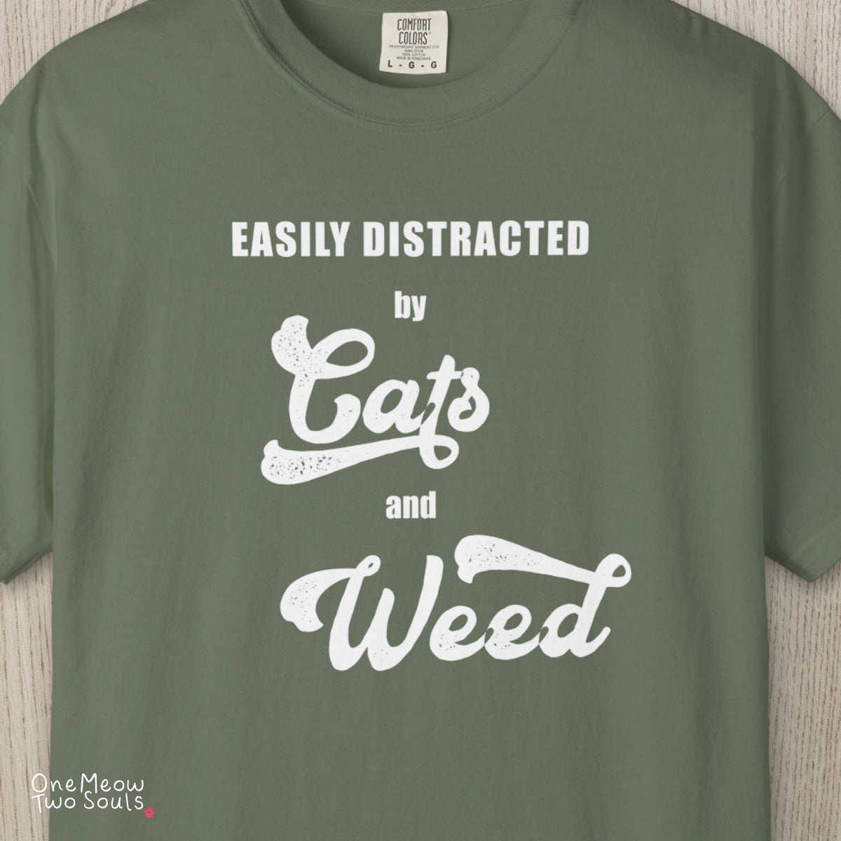 Moss colored Comfort Colors 1717 cotton T-shirt, featuring a "Easily Distracted by Cats and Weed" funny cat design illustration. One Meow Two Souls brand.