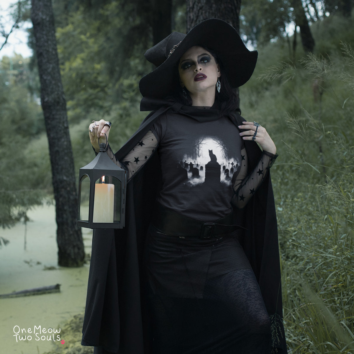 Black colored Comfort Colors 1717 cotton T-shirt, featuring a spooky graveyard Halloween cat design illustration. One Meow Two Souls brand.