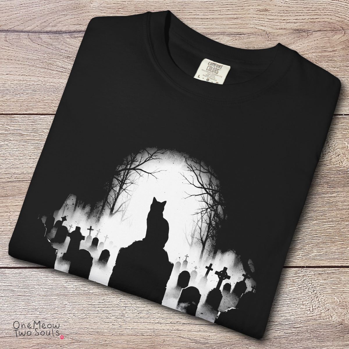 Black colored Comfort Colors 1717 cotton T-shirt, featuring a spooky graveyard Halloween cat design illustration. One Meow Two Souls brand.