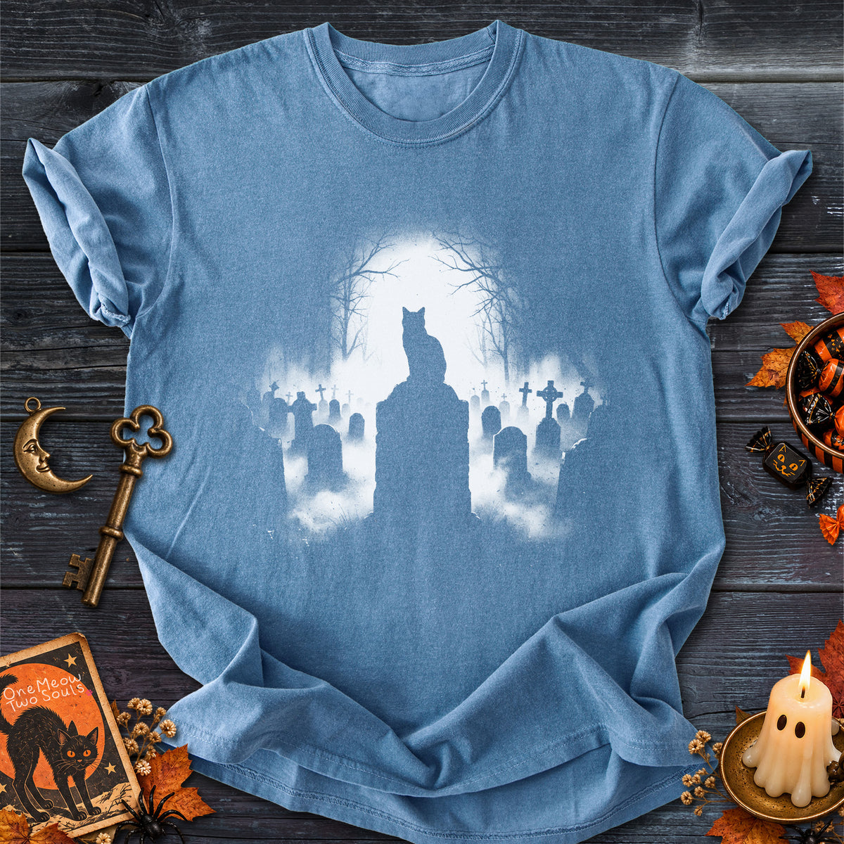 Blue Jean colored Comfort Colors 1717 cotton T-shirt, featuring a spooky graveyard Halloween cat design illustration. One Meow Two Souls brand.