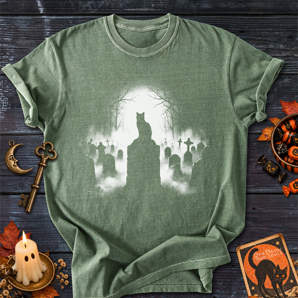 Moss colored Comfort Colors 1717 cotton T-shirt, featuring a spooky graveyard Halloween cat design illustration. One Meow Two Souls brand.