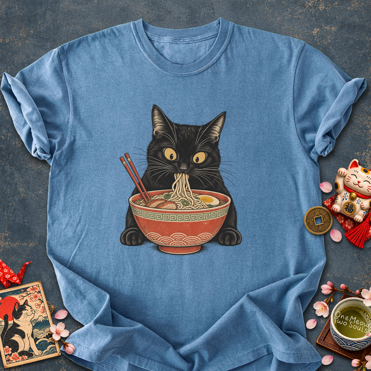 Blue jean colored Comfort Colors 1717 cotton T-shirt, featuring a Black cat eating Japanese ramen noodles. Funny cat design illustration. One Meow Two Souls brand.