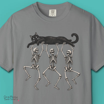 Gray colored Comfort Colors 1717 cotton T-shirt, featuring a Black cat carried by three skeletons funny cat Halloween design illustration. One Meow Two Souls brand.