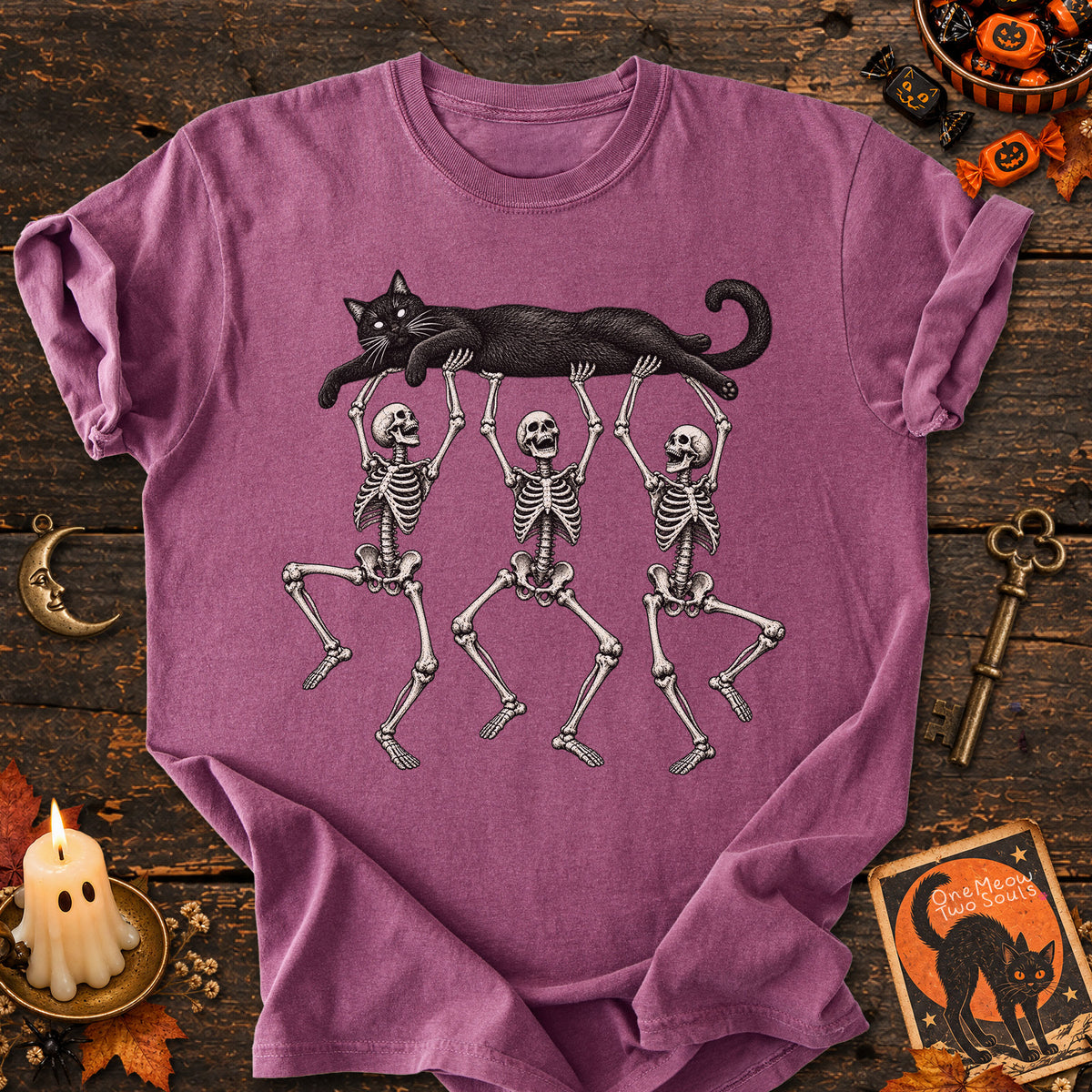 Berry colored Comfort Colors 1717 cotton T-shirt, featuring a Black cat carried by three skeletons funny cat Halloween design illustration. One Meow Two Souls brand.