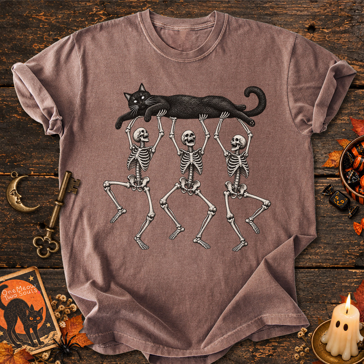 Espresso colored Comfort Colors 1717 cotton T-shirt, featuring a Black cat carried by three skeletons funny cat Halloween design illustration. One Meow Two Souls brand.