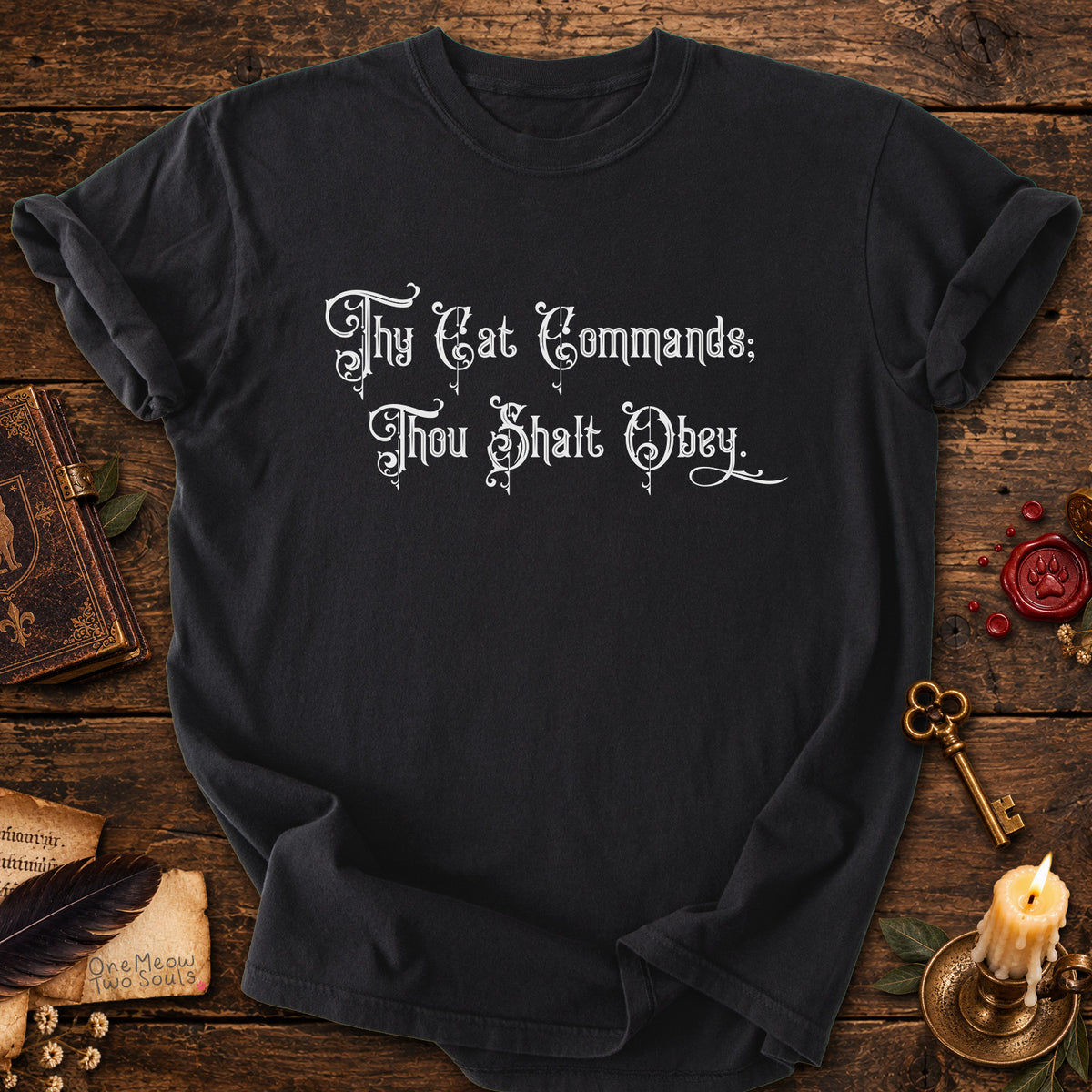 Black colored Comfort Colors 1717 cotton T-shirt, featuring a "Thy Cat Commands. Thou Shalt Obey" funny cat design illustration. One Meow Two Souls brand.
