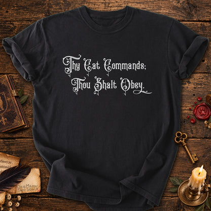 Black colored Comfort Colors 1717 cotton T-shirt, featuring a "Thy Cat Commands. Thou Shalt Obey" funny cat design illustration. One Meow Two Souls brand.