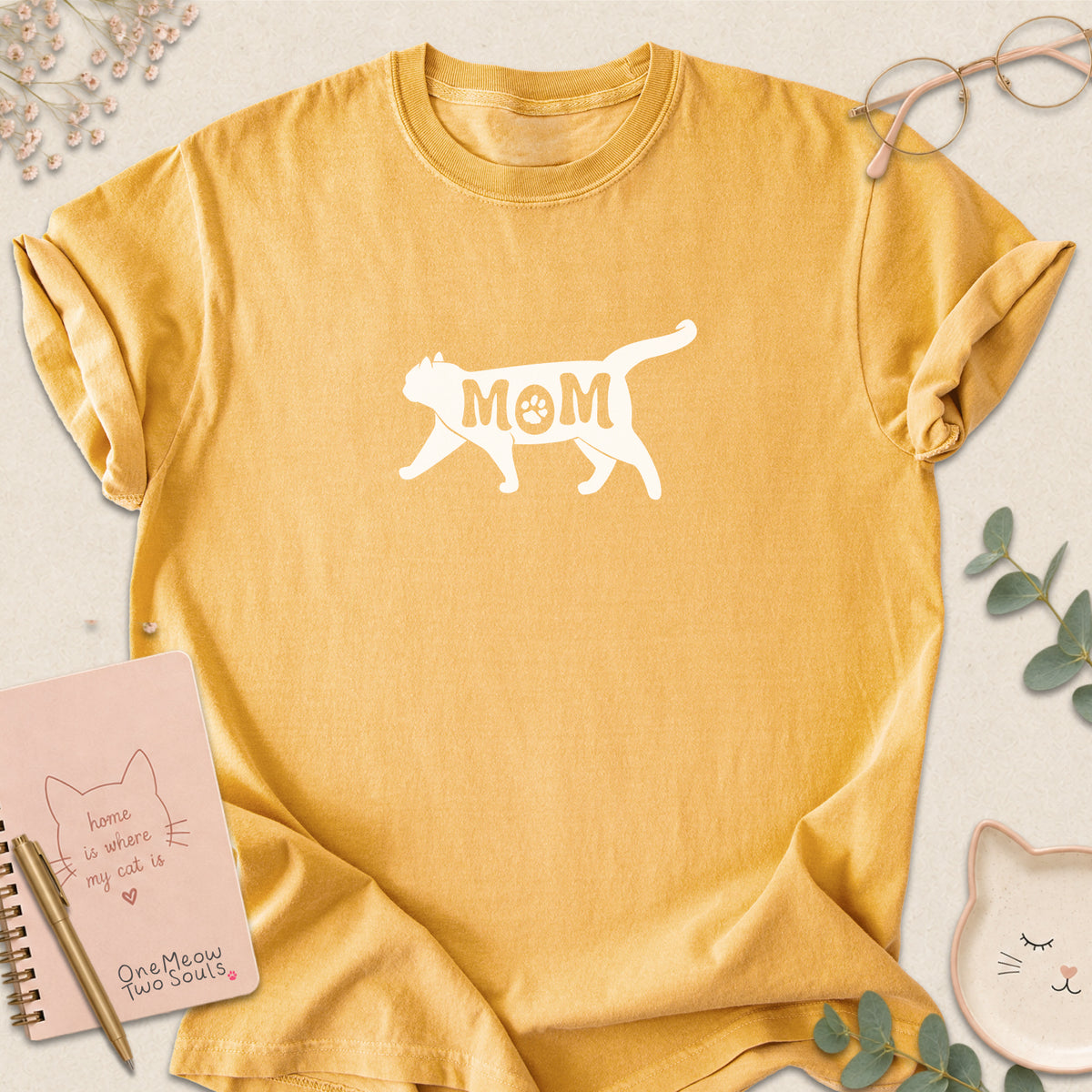 Mustard color Comfort Colors 1717 short-sleeve t-shirt with a white cat silhouette and the word 'MOM' across the chest. One Meow Two Souls brand.